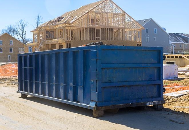 a construction worker holding a heavy load of debris near a residential dumpster